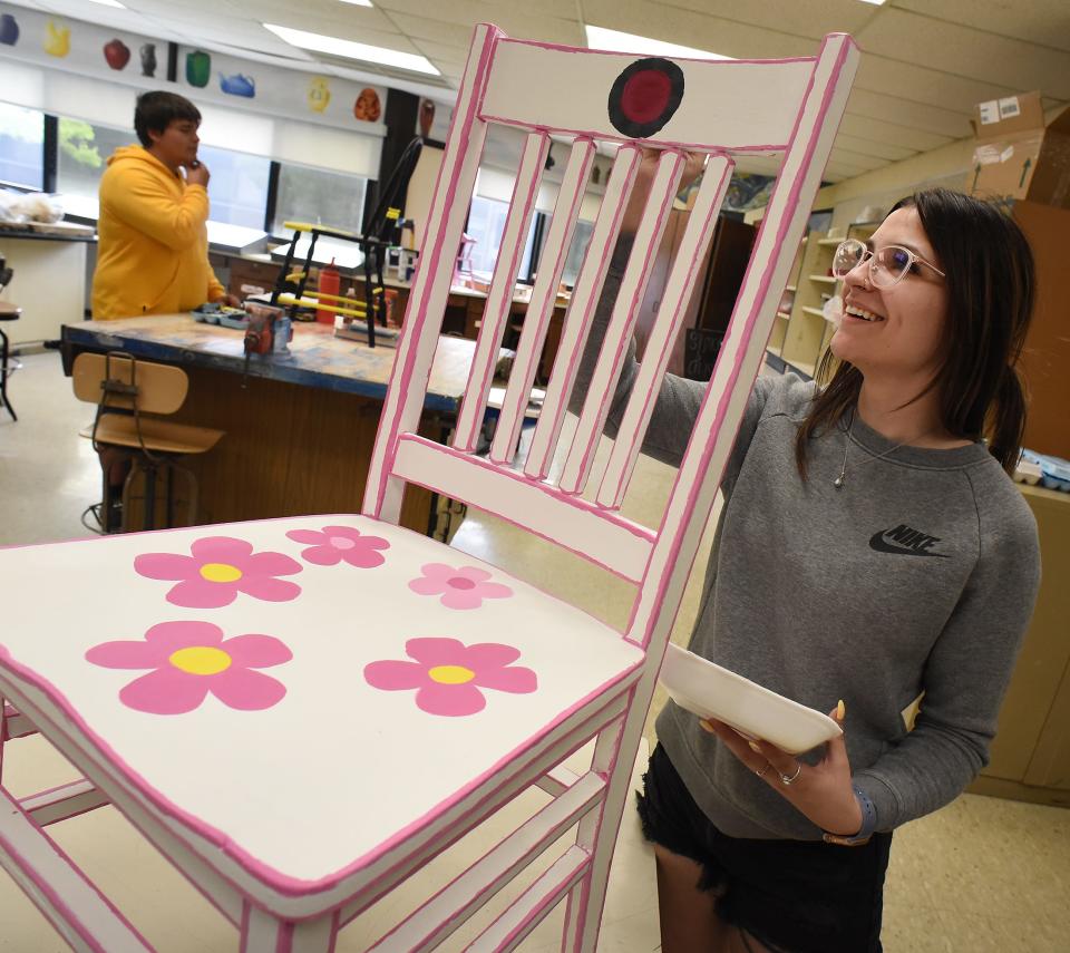 Jefferson High School junior Chloe Reinhardt adds final touches to her pink flower themed chair. Behind is junior Joseph Drew painting a University of Michigan-themed chair. Both chairs will be part of Relay for Life Monroe's auction.