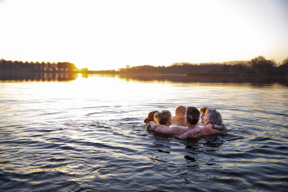 A group of people embracing each other while standing in a calm body of water with the sun setting in the background