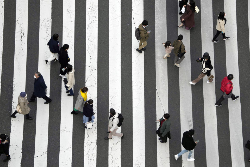 People wearing protective masks to help curb the spread of the coronavirus walk along a pedestrian crossing Monday, Jan. 17, 2022, in Tokyo. (AP Photo/Eugene Hoshiko)