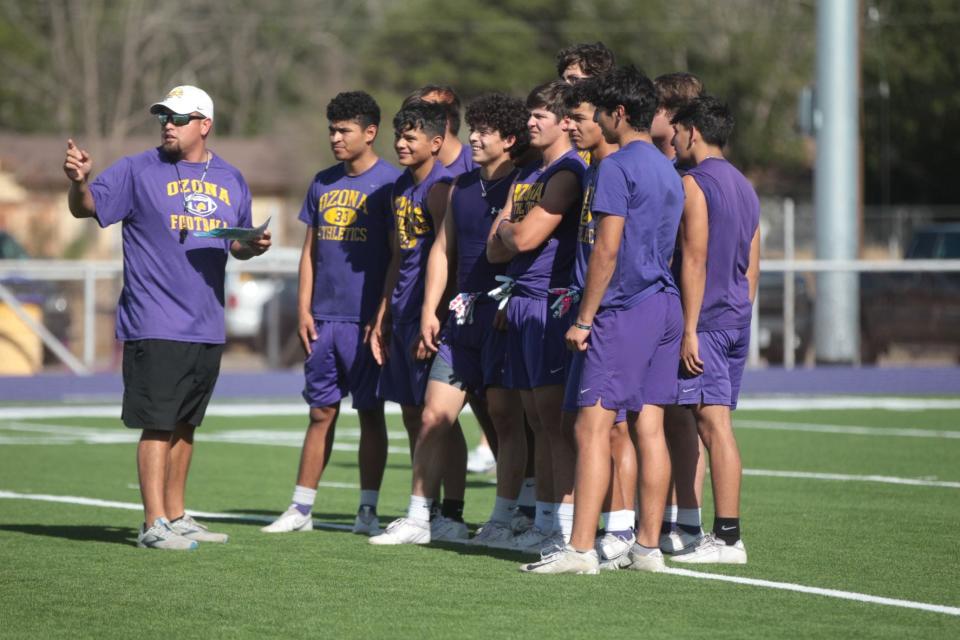 Ozona High School's Rigo Treto (center) smiles as he and his teammates listen to instructions from assistant coach Daniel Cruz during a workout Monday, Aug. 1, 2022, at Lion Stadium in Ozona.