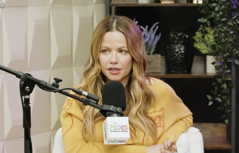 Sasha Pieterse speaking into a microphone during an interview on Pretty Little Liars: True Crime. She is wearing a patterned long-sleeve sweater