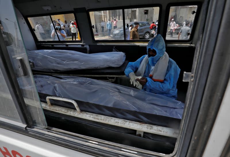 FILE PHOTO: A man wearing a protective suit sits next to the bodies of the victims of the coronavirus disease (COVID-19) inside an ambulance at a mortuary of a COVID-19 hospital in Ahmedabad