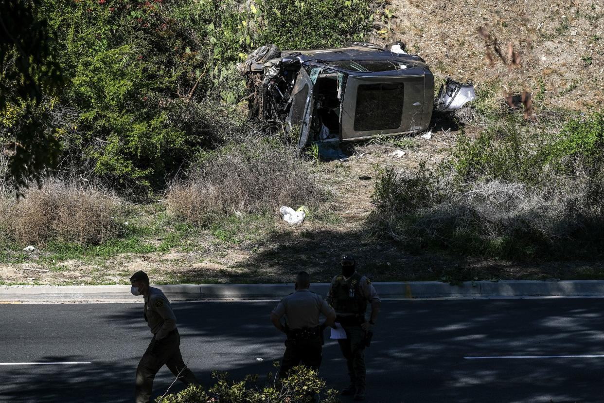 Law enforcement officers watch as a vehicle rests on its side after a rollover accident involving golfer Tiger Woods along a road in the Rancho Palos Verdes suburb of Los Angeles on Tuesday, Feb. 23, 2021.