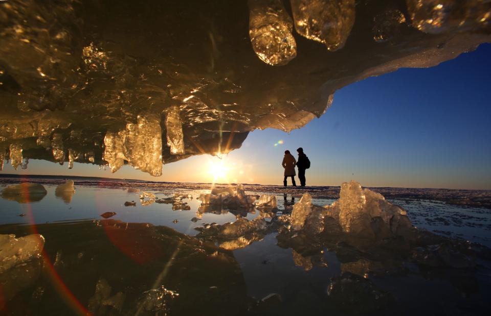 Ruyuan Yang (left) from  Xishuangbanna, China and her friend, Xudung Chang, a Western Michigan University student from Mongolia, are seen through ice formations as the sun begins to set on March 9, 2015.  For the second straight year, the Apostle Islands ice caves were accessible due to thick ice thanks to the cold winter. In all, 37,802 people made the hike to see the formations.