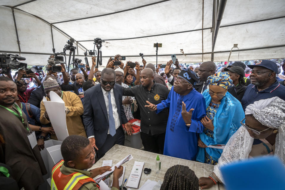 Presidential candidate Bola Tinubu of the All Progressives Congress, center-right, accompanied by his wife, Oluremi Tinubu, gestures as he struggles to cast his vote due to the crowd of media, in the presidential elections in Lagos, Nigeria, Saturday, Feb. 25, 2023. Voters in Africa's most populous nation are heading to the polls Saturday to choose a new president, following the second and final term of incumbent Muhammadu Buhari. (AP Photo/Ben Curtis)