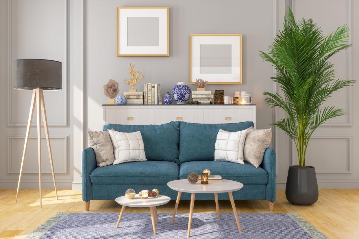 Living room with blue couch, decorative items, blue rug and two picture frames on gray walls, two coffee tables, sunlight shining from left side