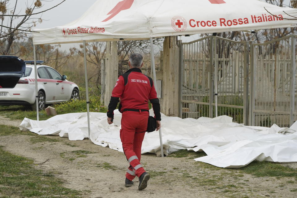 An Italian Red Cross volunteer walks by covered bodies of victims from a capsized boat at a beach near Cutro, southern Italy, Sunday, Feb. 26, 2023. Rescue officials say an undetermined number of migrants have died and dozens have been rescued after their boat broke apart off southern Italy. (Antonino Durso/LaPresse via AP)
