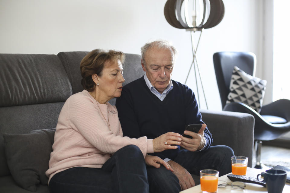 Senior couple in their living room, looking at the phone as government releases coronavirus Whatsapp and iPhone app