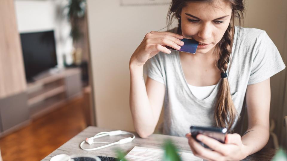 Young woman with braided hair sitting by the table, looking on her smart phone.