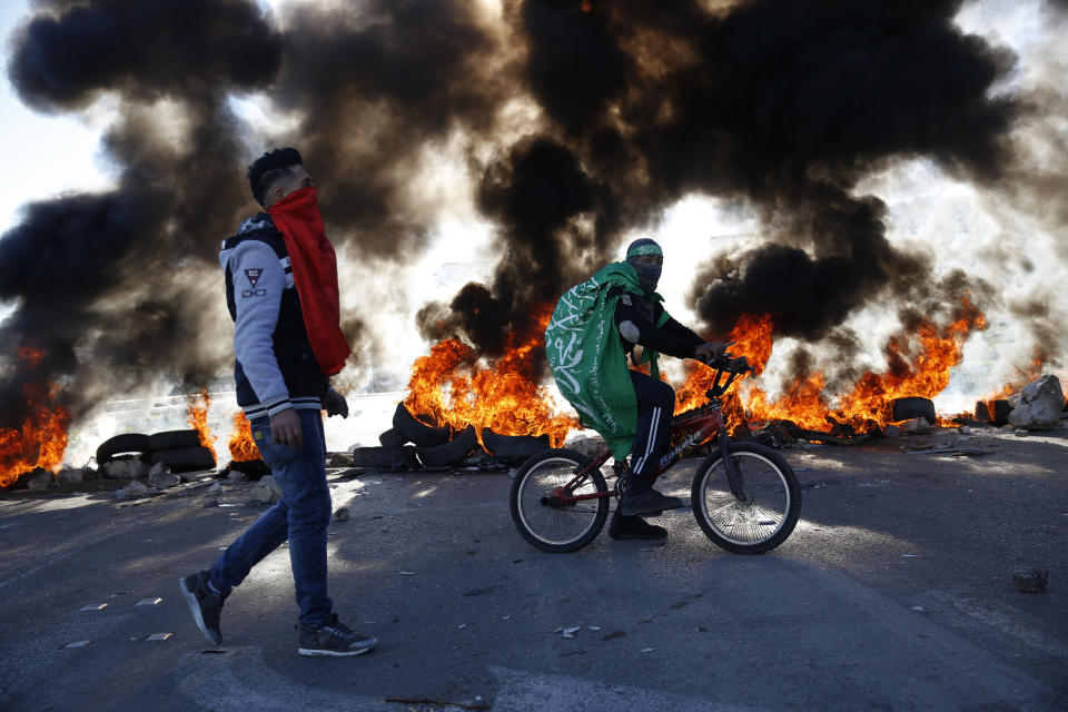 Palestinian wrapped in Hamas flag rides a bike during clashes with Israeli troops at the Hawara checkpoint, south of the West Bank city of Nablus, Friday, Dec. 14, 2018. (AP Photo/Majdi Mohammed)