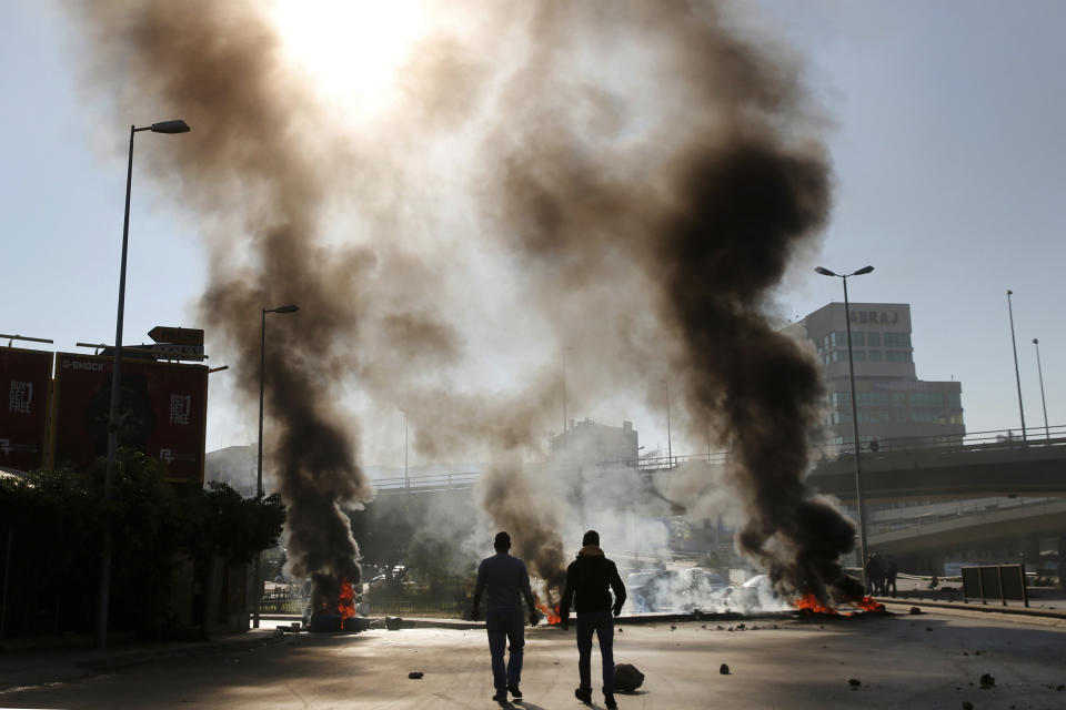 Two men walk near burning tires set on fire by anti-government protesters during ongoing protests after weeks of calm in Beirut, Lebanon, Tuesday, Jan. 14, 2020. Protesters blocked several roads around the capital and in other areas on Tuesday in renewed rallies, after a brief hiatus, against the ruling elite who have failed to address the economy's downward spiral. (AP Photo/Hussein Malla)