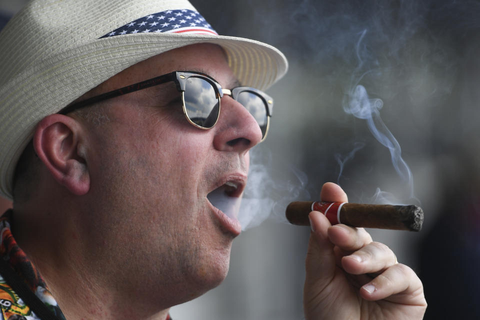 A man smokes a cigar ahead of the Preakness Stakes horse race at Pimlico Race Course, Saturday, May 15, 2021, in Baltimore. (AP Photo/Will Newton)