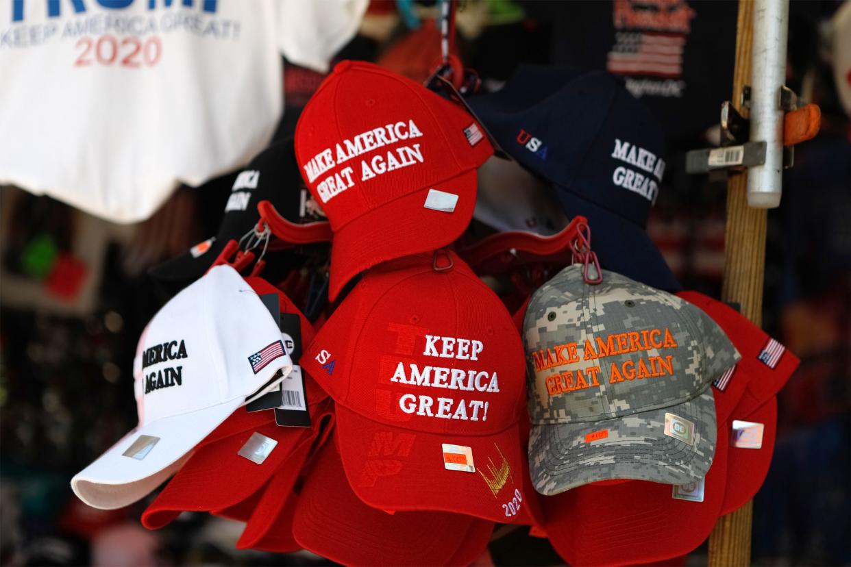 Closeup of Donald J. Trump hats hanging for sale at a street vendor with Trump shirts hanging in the background