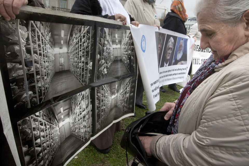 Munira Subasic of the Mothers of Srebrenica, right, and other protestors hold pictures of exhumed bodies from mass graves and pictures of former Bosnian Serb leader Radovan Karadzic outside the building which houses the International Residual Mechanism for Criminal Tribunals in The Hague, Netherlands, Wednesday, March 20, 2019. Nearly a quarter of a century since Bosnia's devastating war ended, Karadzic is set to hear the final judgment on whether he can be held criminally responsible for unleashing a wave of murder and destruction. United Nations appeals judges will on Wednesday rule whether to uphold or overturn Karadzic's 2016 convictions for genocide, crimes against humanity and war crimes, as well as his 40-year sentence. (AP Photo/Peter Dejong)