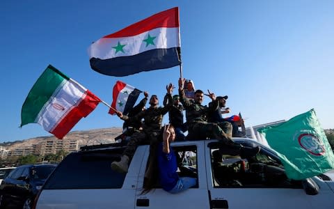 Syrian government supporters wave Syrian, Iranian and Russian flags as they chant slogans against U.S. President Trump during demonstrations following a wave of U.S., British and French military strikes - Credit: AP