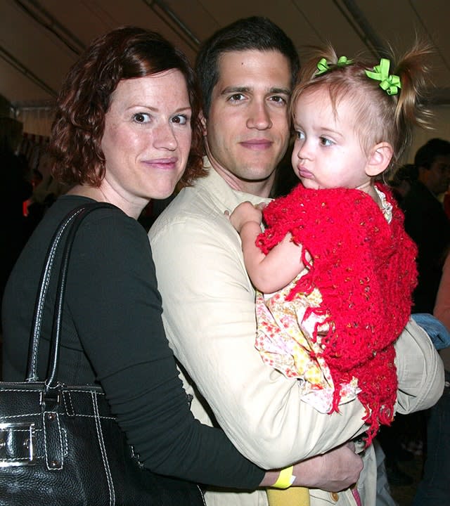 Molly RIngwald in black hugs her boyfriend Panio Gianopoulos in a cream sweater who holds their daughter Mathilda in a red dress