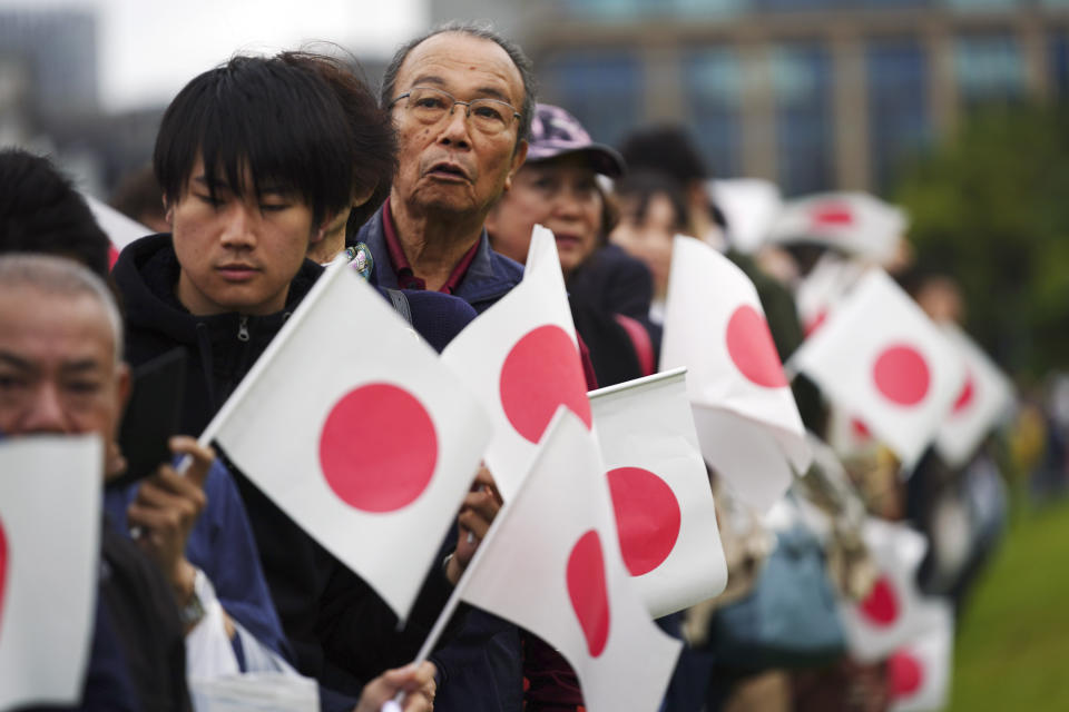 Holding nationals flags, people line up and wait outside of the Imperial Palace during the enthronement ceremony for Emperor Naruhito Tuesday, Oct. 22, 2019, in Tokyo. (AP Photo/Eugene Hoshiko)