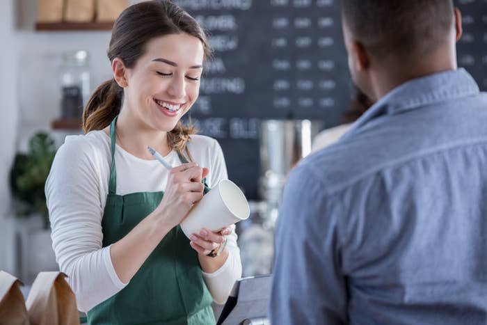 A barista smiling and writing an order on the cup