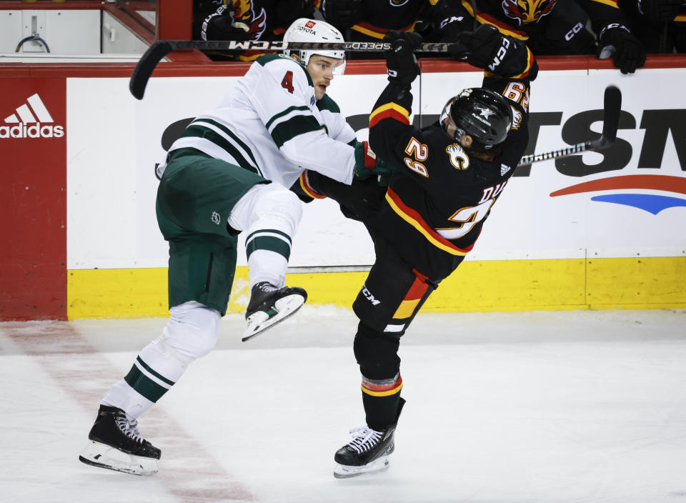 Minnesota Wild defenceman Jon Merrill, left, checks Calgary Flames forward Dillon Dube during the third period of an NHL hockey game in Calgary, Alberta, Tuesday, Dec. 5, 2023. (Jeff McIntosh/The Canadian Press via AP)