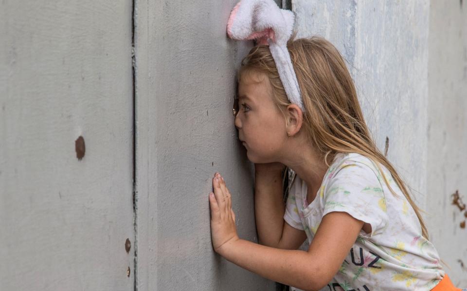 Anhelina looks through a shrapnel hole in a fence after a Russian military strike in Mykolaiv - STRINGER/REUTERS