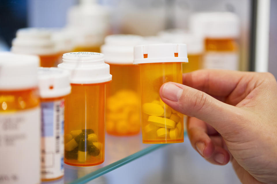 Close-up of a hand holding a prescription pill bottle, surrounded by other similar bottles on a shelf, symbolizing healthcare and medication management