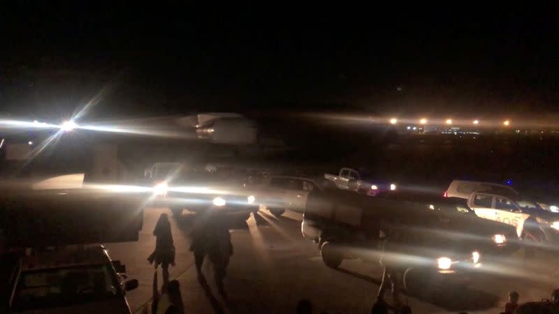 People walk past vehicles on the tarmac towards a plane at the airport in Kabul