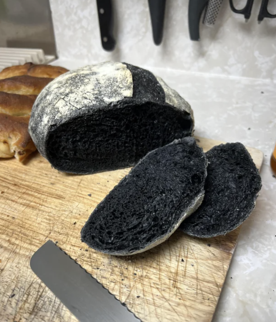 A loaf of charcoal bread is being cut