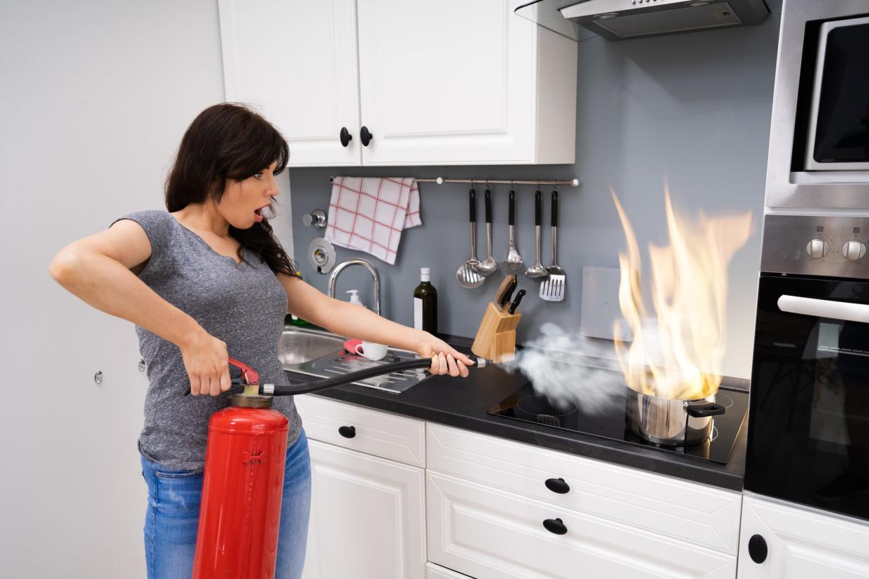 Woman Using Fire Extinguisher To Stop Fire On Burning Cooking Pot In The Kitchen