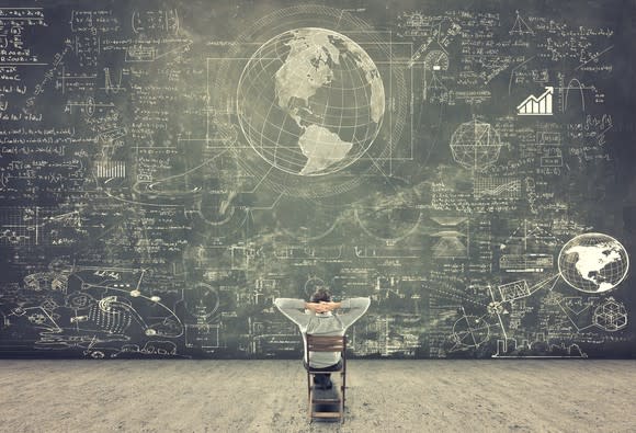 A man looking at lots of information on a giant chalkboard.