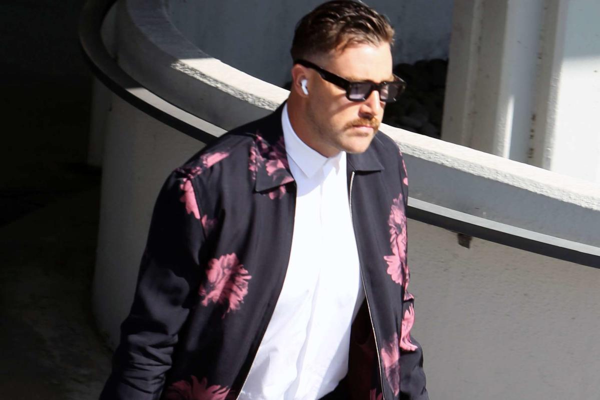 Travis Kelce hugs flowers wearing a pink floral jacket as he arrives at the Kansas City Chiefs game in Los Angeles