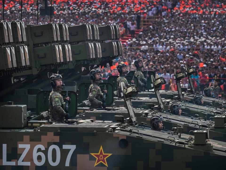 Chinese soldiers sit atop mobile rocket launchers, with crowds of people in the background.