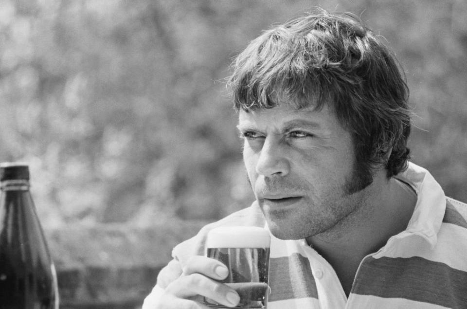 a black and white photo of oliver reed drinking a beer