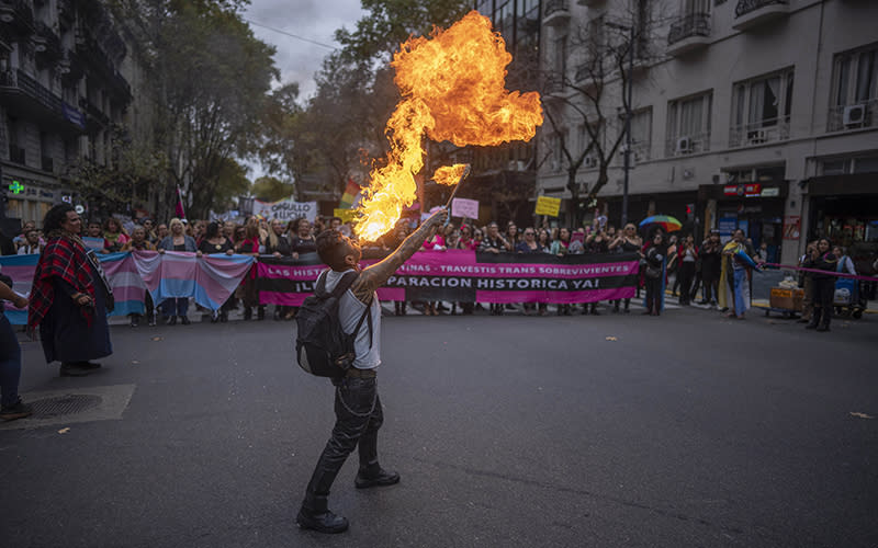 In the background, members of the transgender community march toward Congress during a protest while in the foreground a protester breathes fire