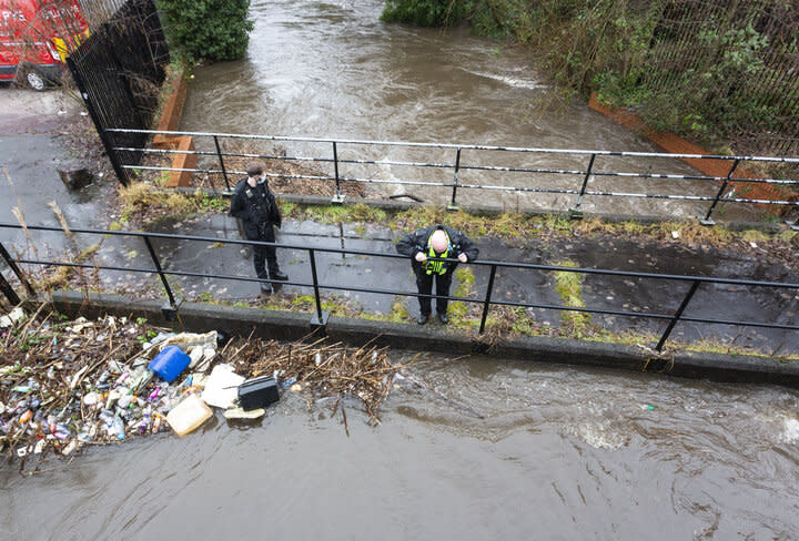 Police officers patrol a submerged bridge along the River Roch, in Greater Manchester.