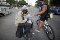 Andrés Burgos, un publicista de 55 años, le da un paquete de arepas o empanadas de harina de maíz a un hombre que pide limosna en un semáforo en Caracas, Venezuela, el martes 20 de octubre de 2020. (AP Foto/Ariana Cubillos)