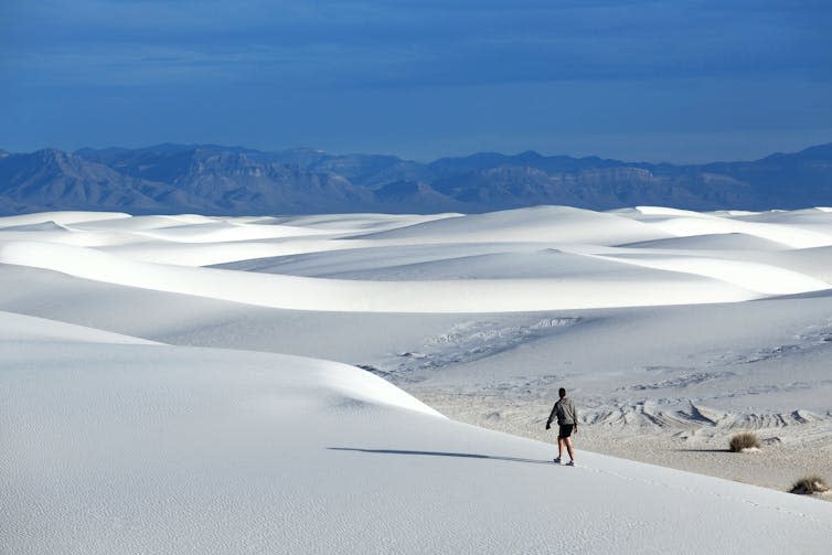 Man walks on white sand dunes, mountains in the background