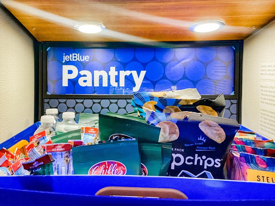 A blue basket of snacks and water bottles on a JetBlue flight.