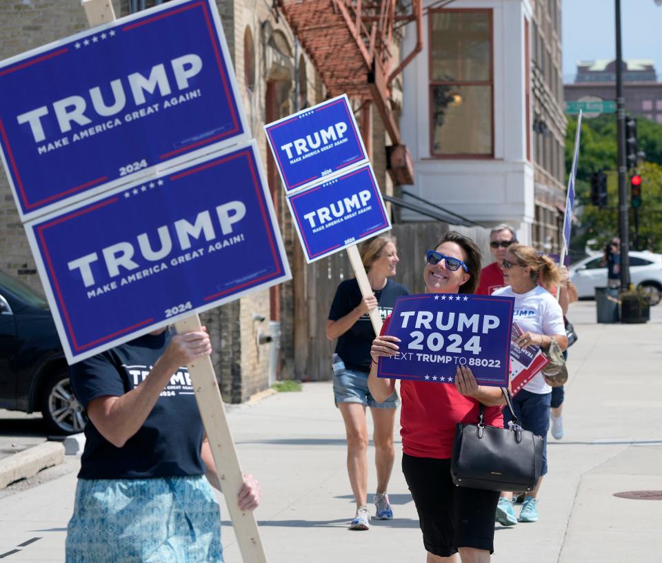 Trump supporters walk with signs near Fiserv Forum as work is done Tuesday in preparation for the Aug. 23 Republican presidential debate in Milwaukee.