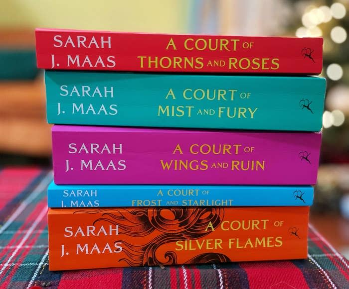 A stack of Sarah J. Maas books from "A Court of Thorns and Roses" series on a plaid surface