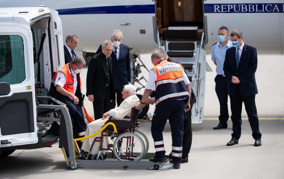 Former pope Benedict XVI (C) sitting in a wheelchair is helped to leave a bus and to get into the plane as his private secretary Georg Gaenswein (3rd L) and Bavaria's State Premier Markus Soeder (R) look on, at the airport in Munich, southern Germany, before the former pope's departure on June 22, 2020. - Former pope Benedict XVI returns to the Vatican from Germany, where he was visiting his sick brother. (Photo by Sven Hoppe / POOL / AFP) (Photo by SVEN HOPPE/POOL/AFP via Getty Images)