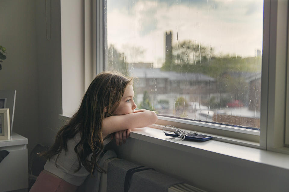 Sad girl looking out of the window at home