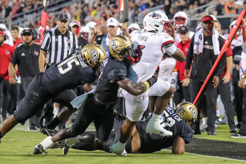 Sep 9, 2022; Orlando, Florida, USA; Louisville Cardinals tight end Marshon Ford (5) is tackled by UCF Knights linebacker Jason Johnson (15) and defensive back Divaad Wilson (9) during the first quarter at FBC Mortgage Stadium. Mandatory Credit: Mike Watters-USA TODAY Sports