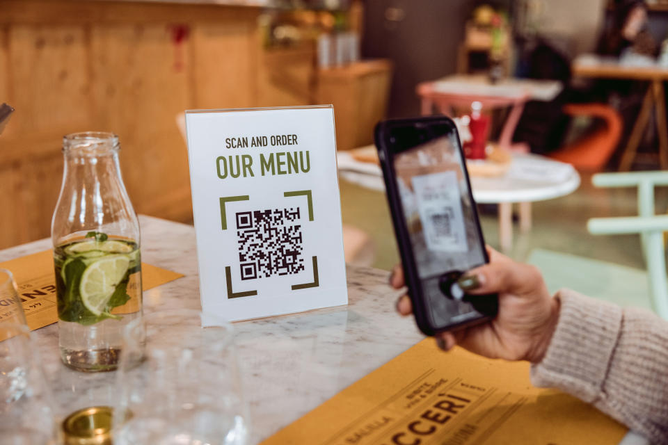 Person scanning a QR code on a "Scan and Order OUR MENU" sign with a smartphone in a restaurant setting