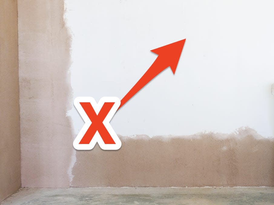 Brown wall with center painted over with white paint and white stool in front to the right. Red X and arrow pointing to white painted part of wall