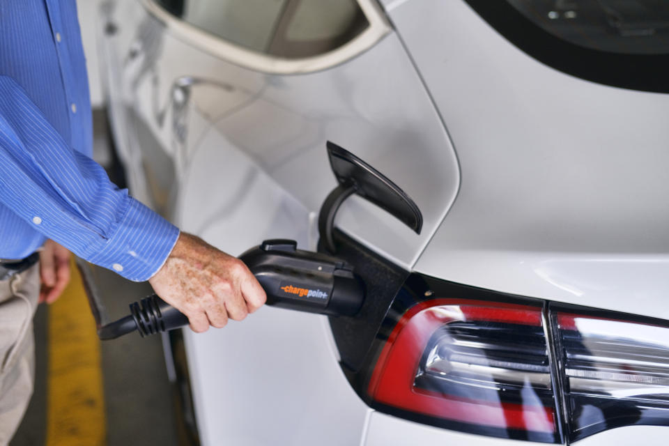 FILE - In this Oct. 16. 2019, file photo a driver plugs in the Charge Point electric plug into his Tesla car at a parking garage in downtown Los Angeles. Experts expect most new cars sold in 2030 to be electric. The Biden administration promised 550,000 charging stations to help with the transition to electric cars.(AP Photo/Richard Vogel, File)