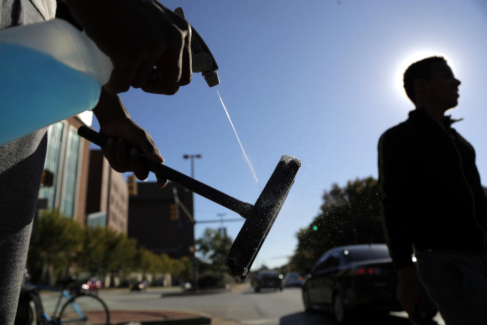 In a photo taken Thursday, Oct. 24, 2019, Jerome Holloway, left, sprays his squeegee as he and another teenager walks by as they work a corner in Baltimore. A debate over Baltimore's so-called squeegee kids is reaching a crescendo as the city grapples with issues of crime and poverty and a complicated history with race relations. Officials estimate 100 squeegee kids regularly work at intersections citywide, dashing into the street as red lights hit to clean windshields in exchange for cash from drivers. (AP Photo/Julio Cortez)