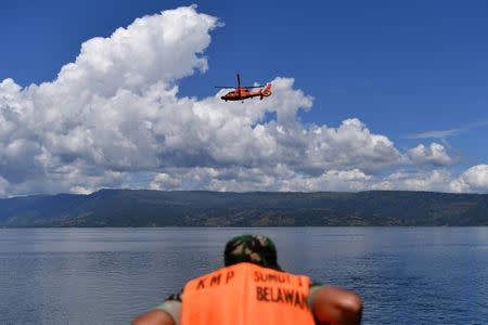 A rescue team member stands as a rescue helicopter flies during a search for missing passengers after a ferry sank last week in Lake Toba in Simalungun, North Sumatra, Indonesia, June 28, 2018. Picture taken June 28, 2018. Antara Foto/Sigid Kurniawan/via REUTERS