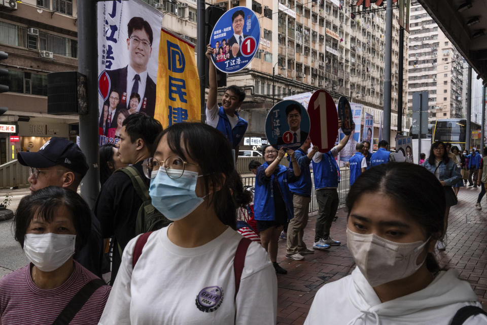 Pedestrians walk past campaigners promoting candidates during the District Council elections in Hong Kong, Sunday, Dec. 10, 2023. Residents went to the polls on Sunday in Hong Kong's first district council elections since an electoral overhaul was implemented under Beijing's guidance of “patriots” administering the city, effectively shutting out all pro-democracy candidates. (AP Photo/Louise Delmotte)