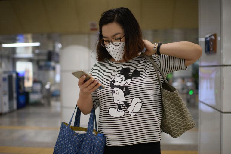 A woman wearing a face masks looks at her phone as she exits a subway station in the popular Myeongdong shopping area in Seoul on June 4, 2015