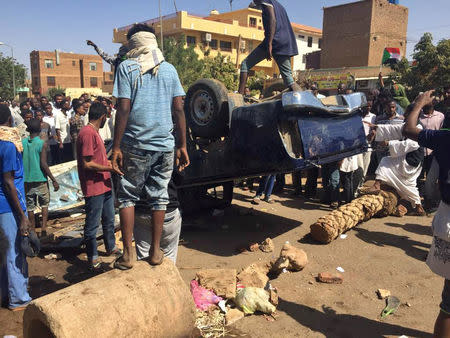 A man stands on top of a car flipped over and damaged by mourners outside the home of a demonstrator who died of a gunshot wound sustained during anti-government protests in Khartoum, Sudan January 18, 2019. REUTERS/Khalid Abdelaziz